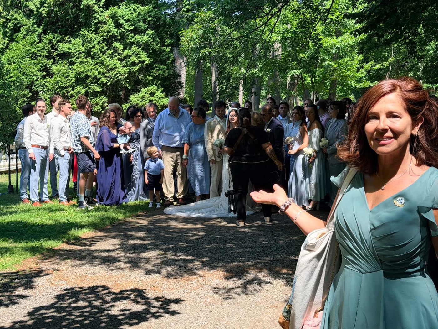 Isabelle Ferland souriante, bras ouverts, devant les mariés et tous les invités réunis dans un parc boisé.