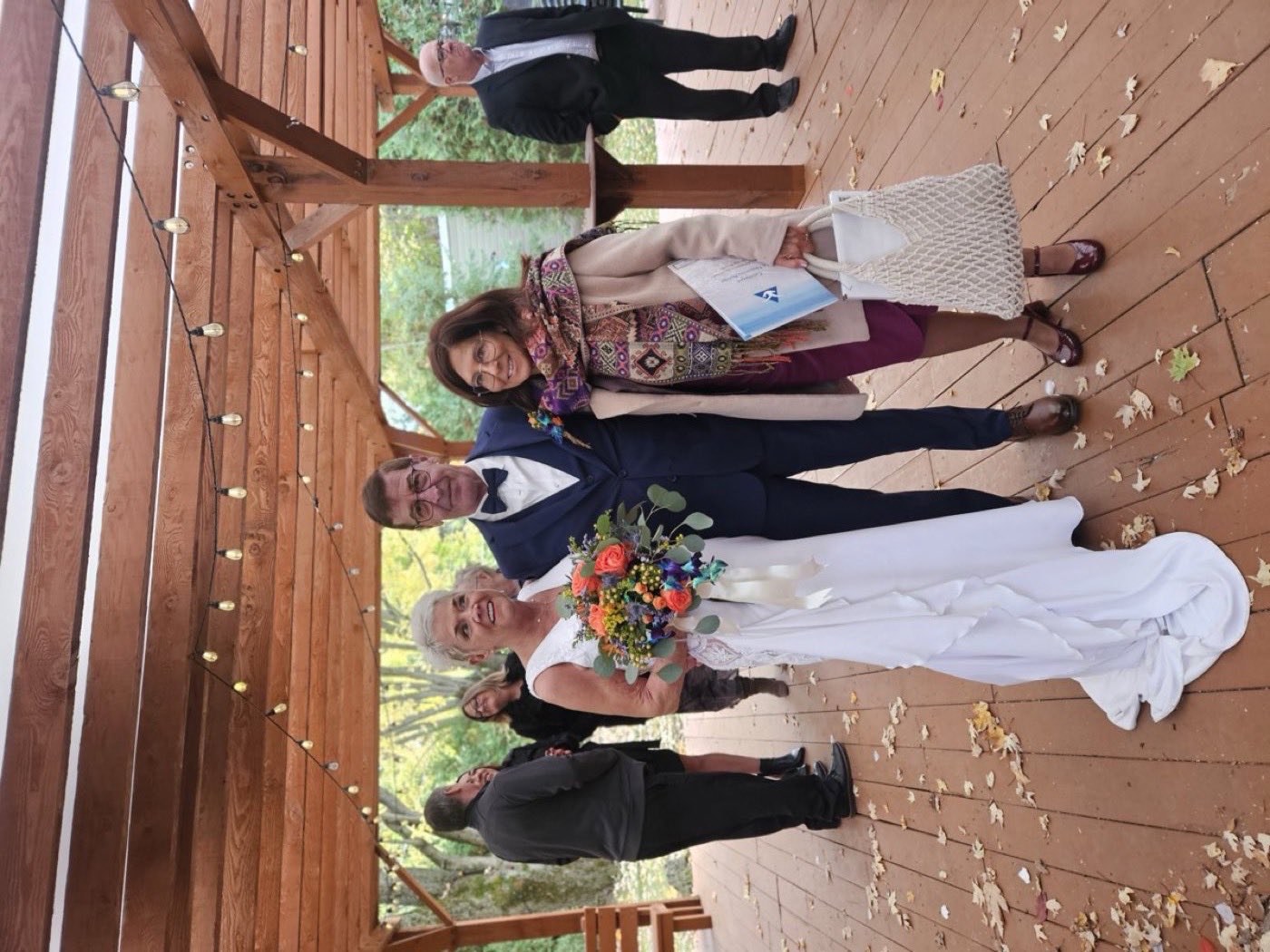 Isabelle Ferland avec les mariés sous une pergola de bois décorée de guirlandes lumineuses, en automne.