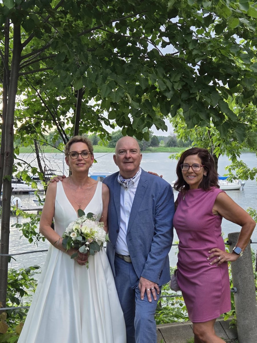 Portrait d’Isabelle Ferland, célébrante, aux côtés d’un couple de mariés au bord de l’eau.
